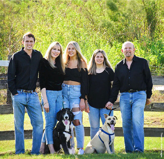Smiling Piller family of five with their two dogs outside with greenery in background.